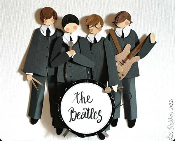 papercut Beatles figures with paper drum set, guitar, microphones, and drumsticks