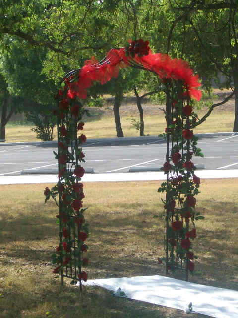 Red silk roses and organza are added to this arch to enahnce wrought iron