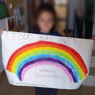 Sale mi pequeña sujetando un cartel donde se ha dibujado un enorme arcoiris y arriba pone Todo irá bien, y abajo Gracias, sanitarior, #yomequedoencasa