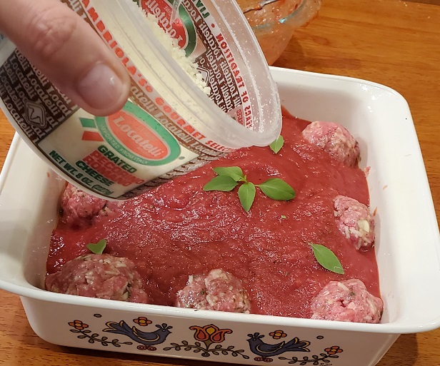 grated cheese on top of a casserole of meatballs with rice