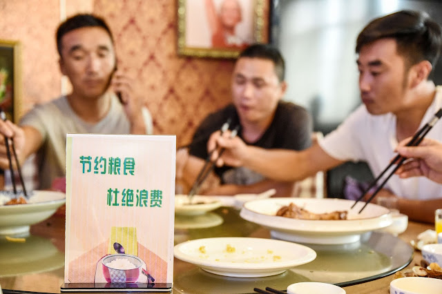 A sign encouraging people not to waste food is displayed on a restaurant table. Chinese hosts often order dishes in excess to show their hospitality.