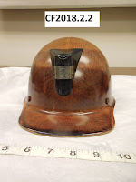 Safety helmet with brown textured coating, short brim, and bracket on front for a lamp - catalog number CF2018.2.2 is at top of photo