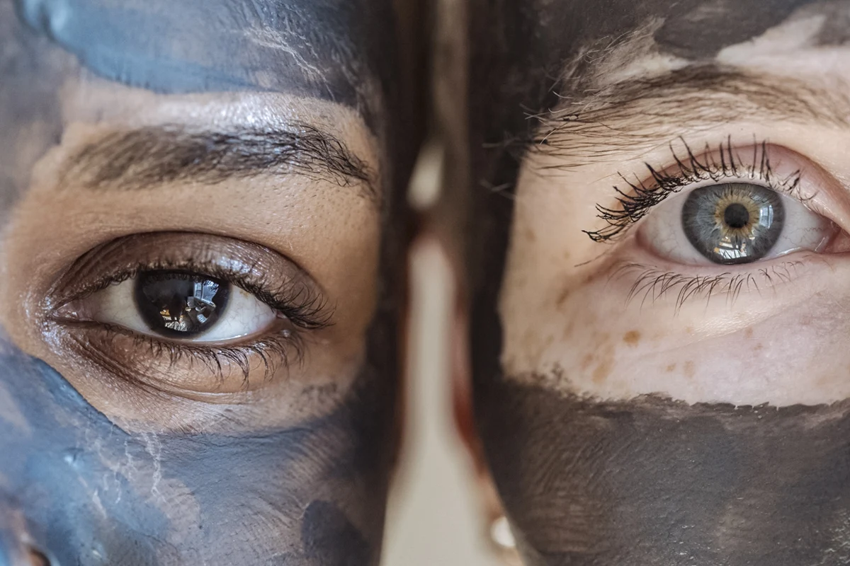 close-up of two female faces with charcoal face mask on the skin