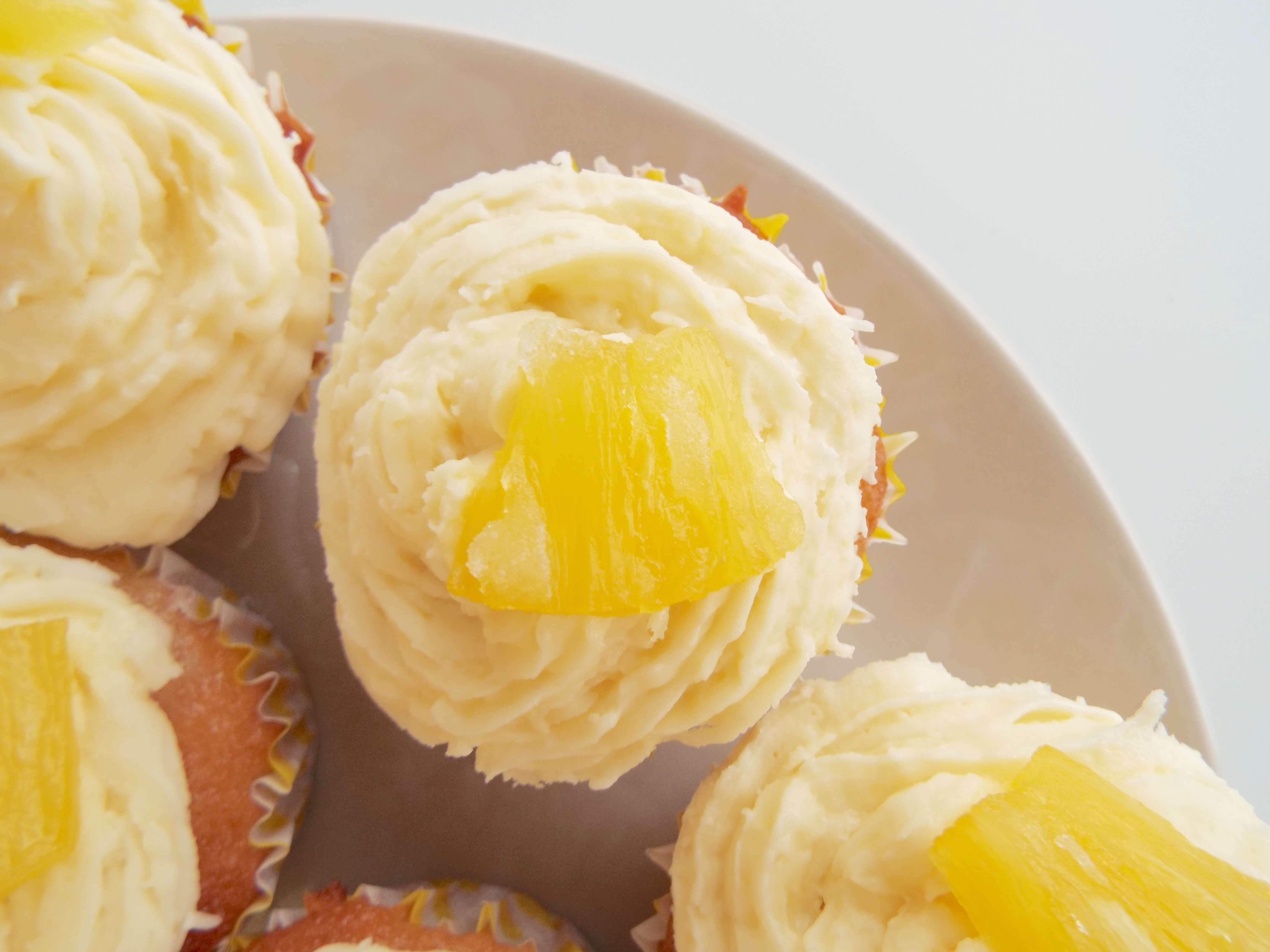 Close up, overhead shot of cupcake with cream coconut icing and sugared pineapple on top.