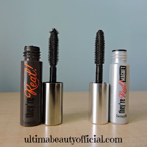 Opened black mini mascara tube with mascara wand. "Benefit They're Real!" printed on it. Next to it, an opened gray mini mascara tube with mascara wand. "Benefit They're Real! Magnet" printed on it.