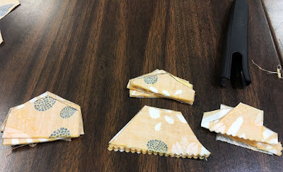 Four small stacks of yellow print fabric, arranged in a squashed diamond. Two stacks are half-hexagons, some point-to-point and some side-to-side; another stack is narrow cut-off points, and the last is random small shapes.