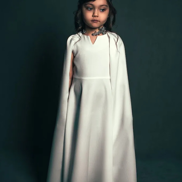 An image of a girl child wearing a long white dress looking very sad.