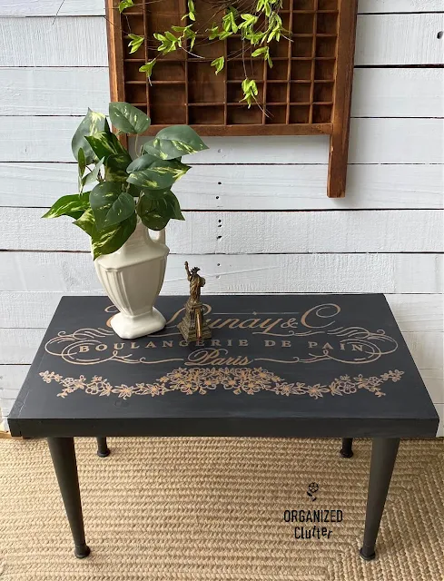 Photo of a thrifted midcentury coffee table painted black with a gold French design transfer.