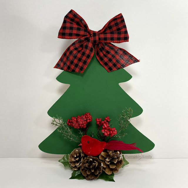 A green wood Christmas tree with a plaid bow, a red bird, berries, and pinecones.