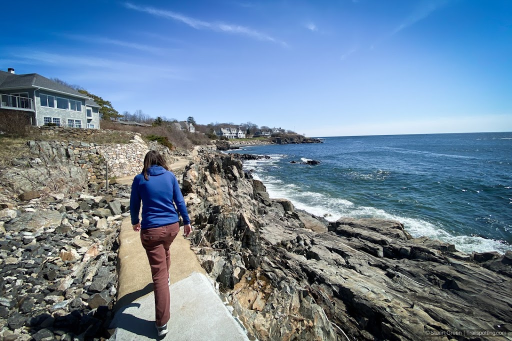 Hiker walking along a narrow cement path by the ocean.