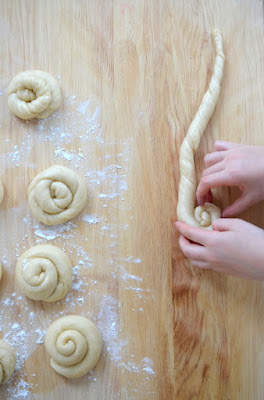 Schnecken aus Hefeteig werden von Kinderhänden auf einem bemehlten Holzbrett geformt.