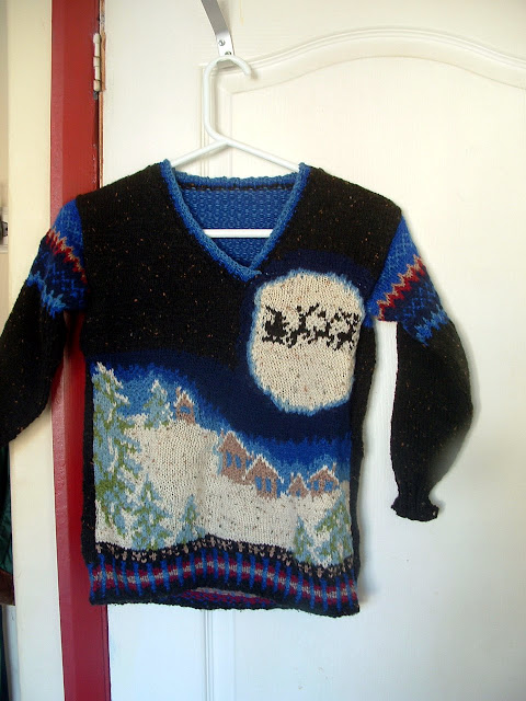 A hand knitted Christmas sweater showing a snowy village under the moon