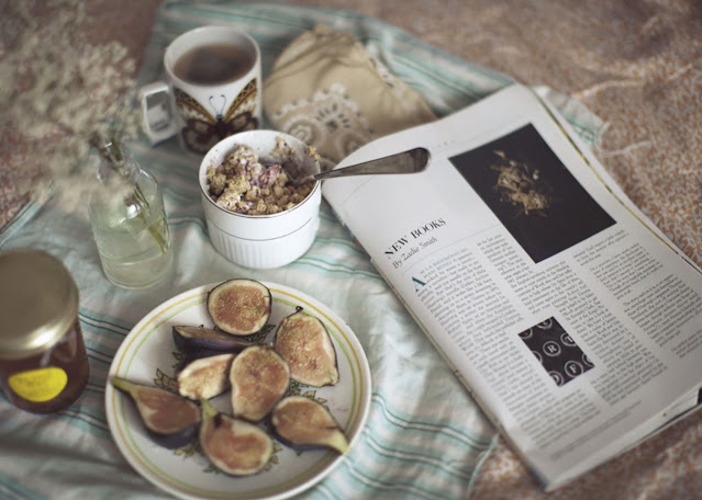 This photo still life shows a beautifully-staged breakfast of figs, yogurt with granola, and tea, next to a magazine open to an article by Zadie Smith titled “New Books.”