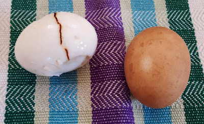 Two hard boiled eggs. One cracked and peeled. The other unpeeled.