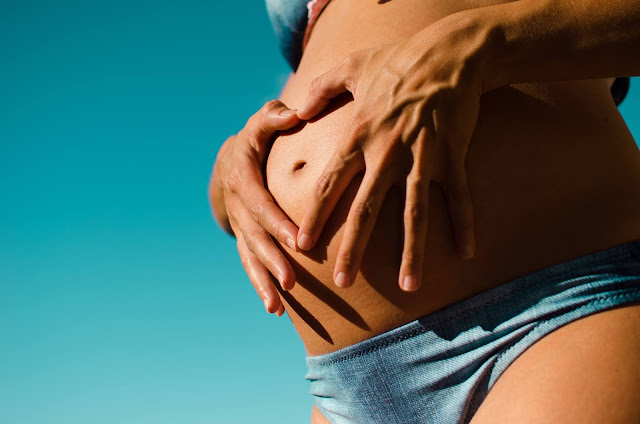 Pregnant lady wearing a bikini with her hands making a heart on her stomach