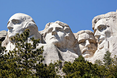 A frontal view of Mount Rushmore which is made oup of four large partial portraits of four Presidents of the United States. They include George Washing,