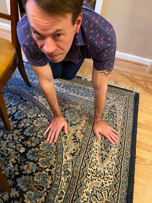 Photo of Alex on all fours on a carpet looking for a puzzle piece. His shirt has tiny lobsters on it.