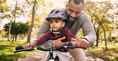 A father holding his son while teaching him to ride a bike.