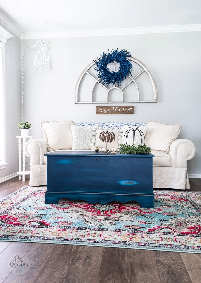 neutral sofa on multicolor rug, blue trunk and blue painted berry wreath on antique arch window