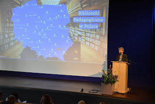 Podkarpacki Kurator Oświaty przemawia ze sceny za mównicą. W tle ekran z wyświetloną mapą Bibliotek Pedagogicznych w Polsce