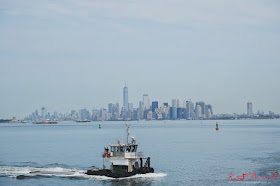 A tug boat Helen Parker, crosses Manhattan Harbor with the Manhattan city skyline and various barges in the distance. Travel photography by Kent Johnson.