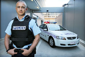 Eric Walsh stand in front of a police car wearing a police vest and uniform