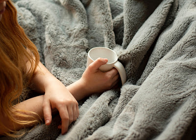 Woman holding a mug under a warm blanket