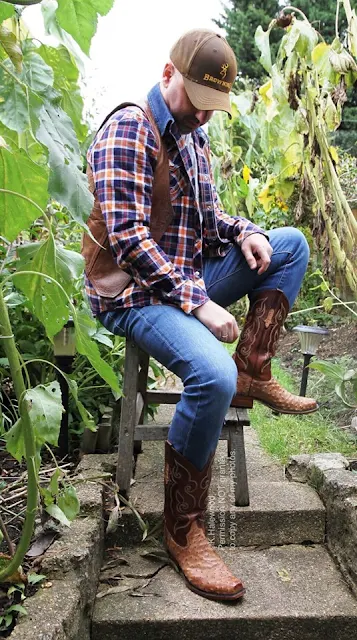 8/11 sitting on a stool in the middle of a cornfield a redneck wearing a John Deere cap, flannel with orange leather blazer over top, blue jeans and cowboy boots which he stares down at seriously