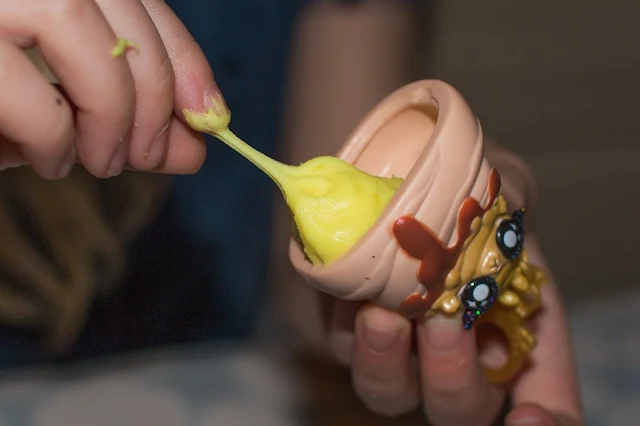A keychain storage container with yellow slime being put inside from drop 3 Poopsie Slime Surprise 