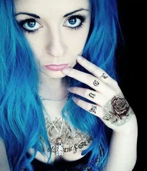 Foto de una joven de cabello azul con mirada melancólica, lleva tatuaje de rosa y letras en la amano