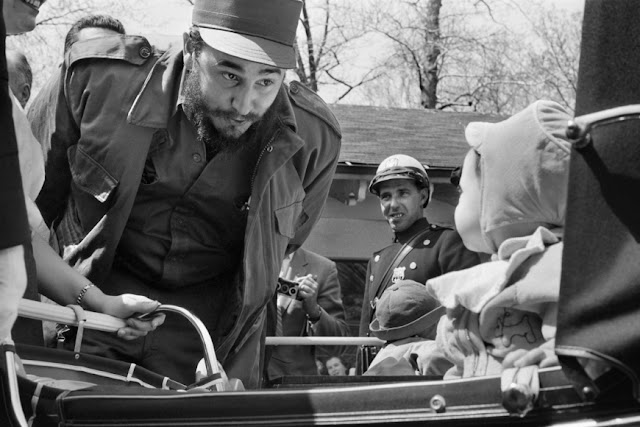 Fidel Castro é visto usando camisa de botão, casaco e boné olhando para uma criança em um carrinho de bebê. Uma mulher é vista parcialmente à esquerda da imagem sorrindo e segurando o carrinho e outras pessoas são vistas no ambiente, dentre as quais um policial sorrindo enquanto olha Fidel Castro. A cena se passa no Central Park na cidade de Nova York.