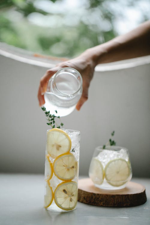 A hand pouring water in a jar half filled with water and half cut lemons