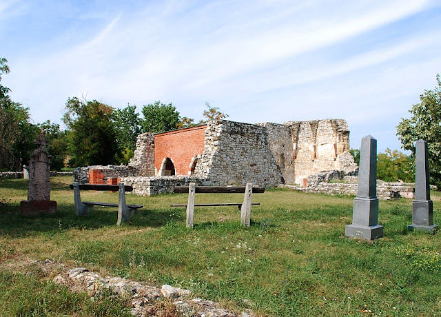 A papsokai templomrom falmaradványai, körülötte temető sírkövei, előtérben két pad.