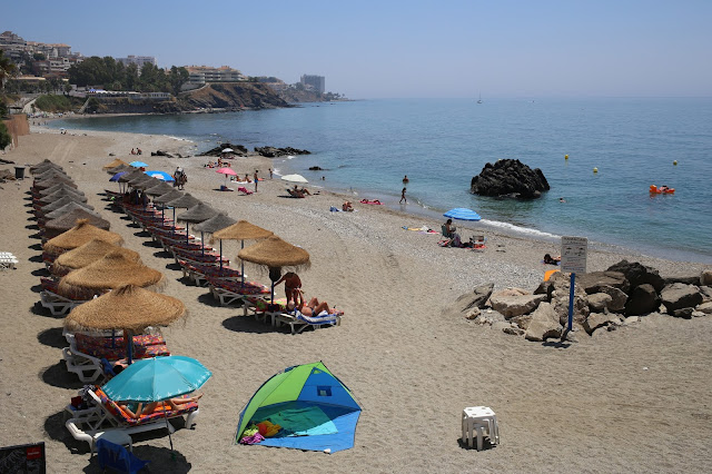Playa con sombrillas de paja y gente de vacaciones.