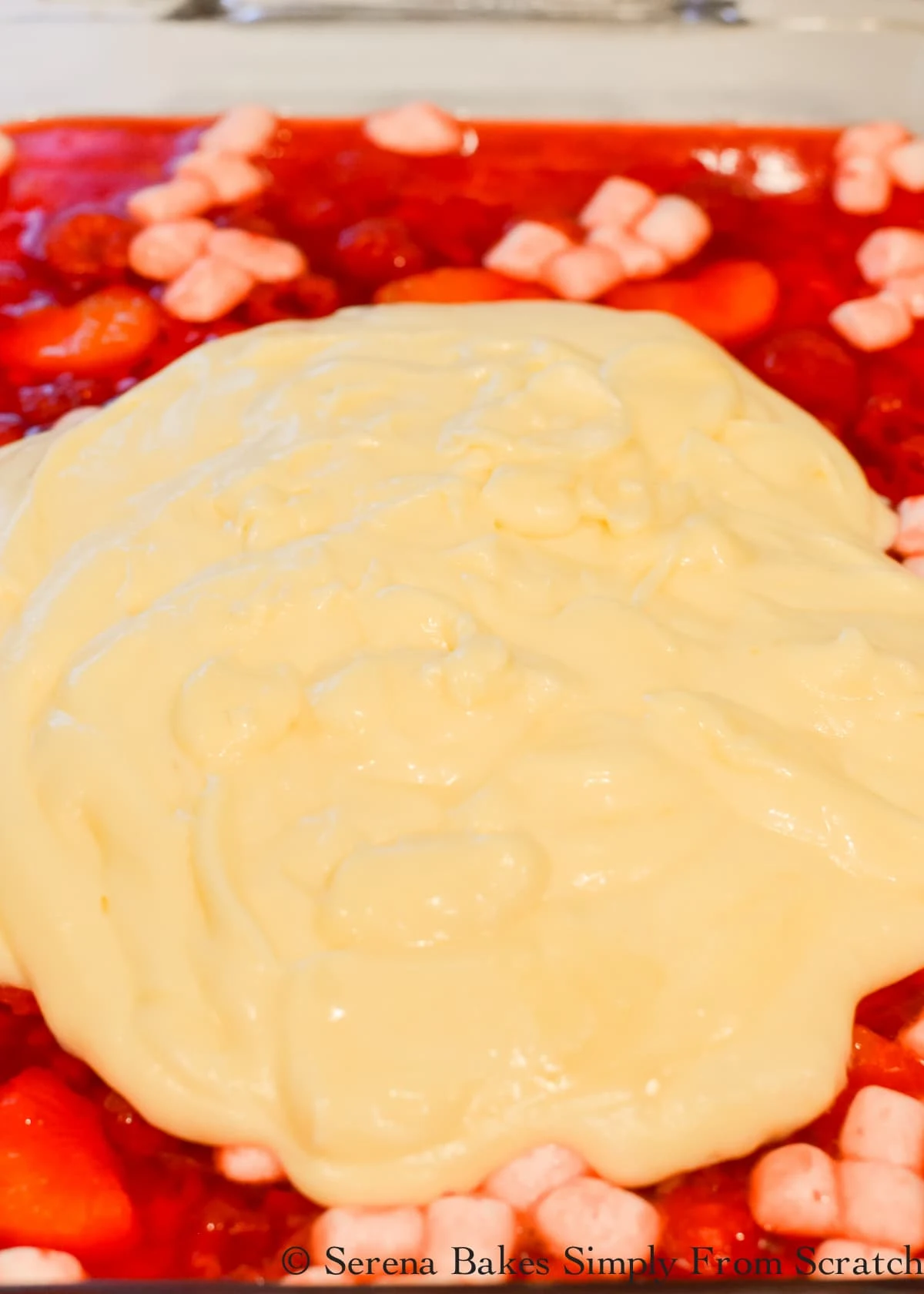 7 Up Raspberry Jello Salad in a glass pan being covered with Pineapple Pudding mixture.