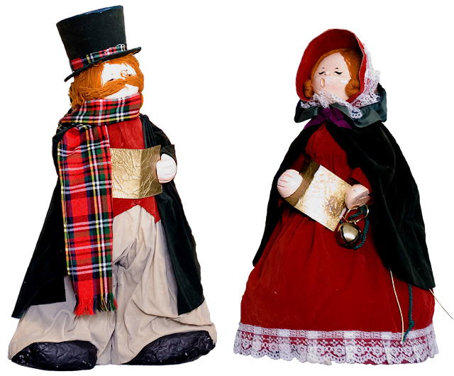 Two vintage papier mache carolers dressed in velvet, he's wearing a tophat and plat scarf, she's wearing a red-velvet dress, green cape and red bonnet.