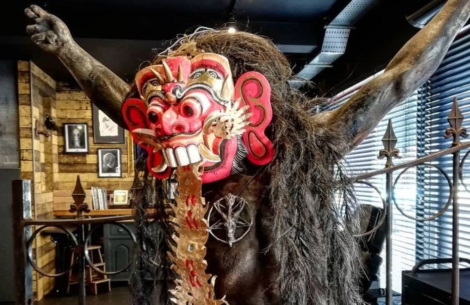  A statue of a leak, a mythological creature from Bali, with a red and green face, sharp teeth, and long black hair.
