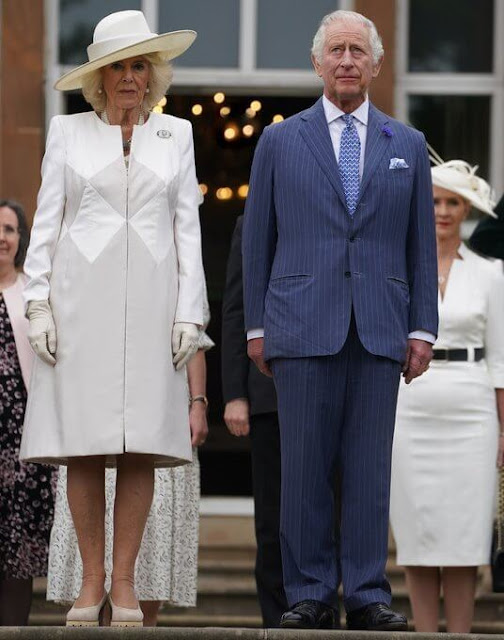 Queen Camilla wore a blue midi dress. The Queen wore an ivory two-tone coat and white midi dress. Coronation Garden in Newtownabbey