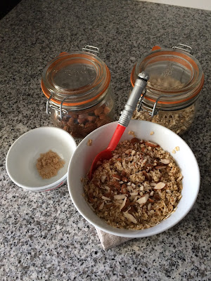 Un bol de flocons d'avoines aux amandes accompagné de deux bocaux en verre avec les ingrédients amande et flocons d'avoine sur plan de travail en granit vue du dessus