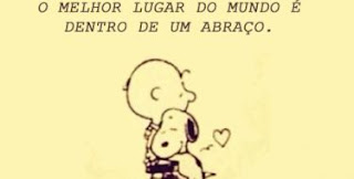 Em um retângulo amarelo claro, ao centro, Charlie Brown e seu cãozinho Snoopy, abraçados e próximo a eles solto no ar, um pequeno coração! No topo, em letras pretas maiúsculas, lê-se: O melhor lugar do mundo é dentro de um abraço. Taí o recado a todos: Um Feliz Dia do Abraço!