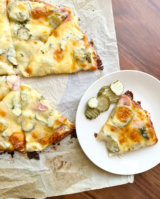 Dill Pickle Pizza on brown parchment paper, with a slice on a white dinner plate with pickles.