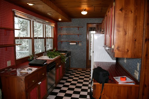 Angela of Fixing it Fancy's kitchen before her remodeling with dark wood cabinets, black and white checker board floor and mismatched wallpaper