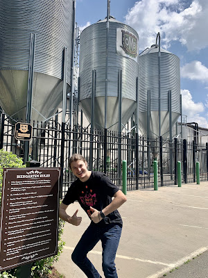 A smiling Andy giving two thumbs up next to a sign of rules listed before entering the Old Mecklenburg brewery.