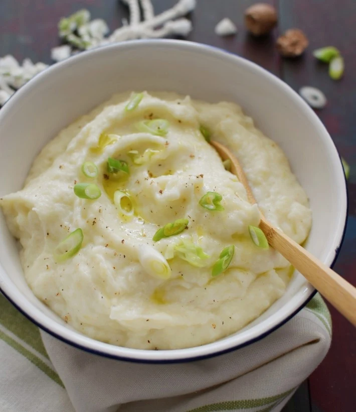 Puré de coliflor cremoso, servido en un tazón, con nuez moscada rallada y cebollines picados en el tope