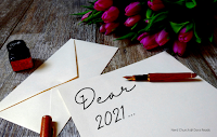 'Dear 2021...' written in fancy writing on a piece of paper, on top of a desk which for some reason also has a bunch of tulips on it