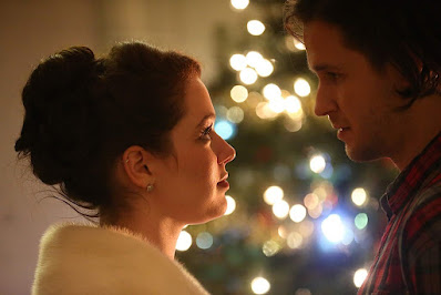 Cassie and Sam looking lovingly at each other in front of a Christmas tree