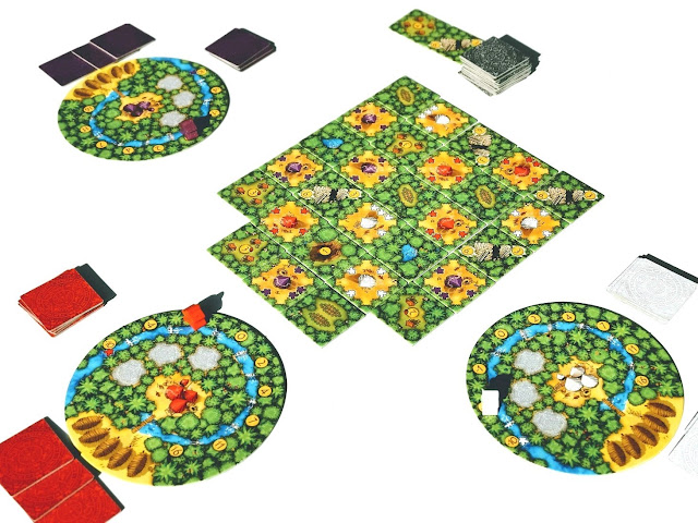 na zdjęciu rozgrywka trzech graczy, na środku stołu wyłożone kafle dżungli i szałasów a na około trzy plansze graczy oraz kafle w ich kolorach