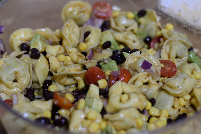 All of the ingredients for the pasta salad tossed together in a bowl.