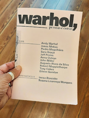 uma mão segurando um Panfleto da exposição Warhol, pessoas e coisas com os nomes de vários artistas