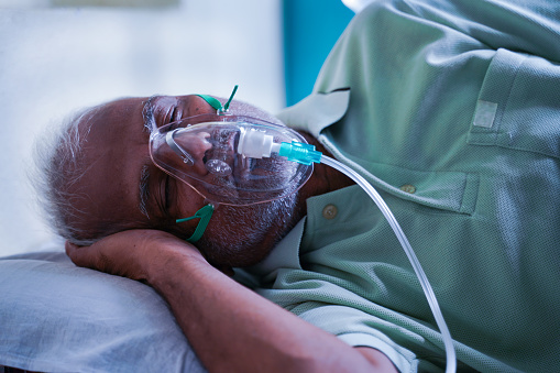Visão lateral de paciente doente idoso respirando em máscara de respirador de oxigênio devido a coronavírus ou infecção viral de falta de ar covid-19 no hospital